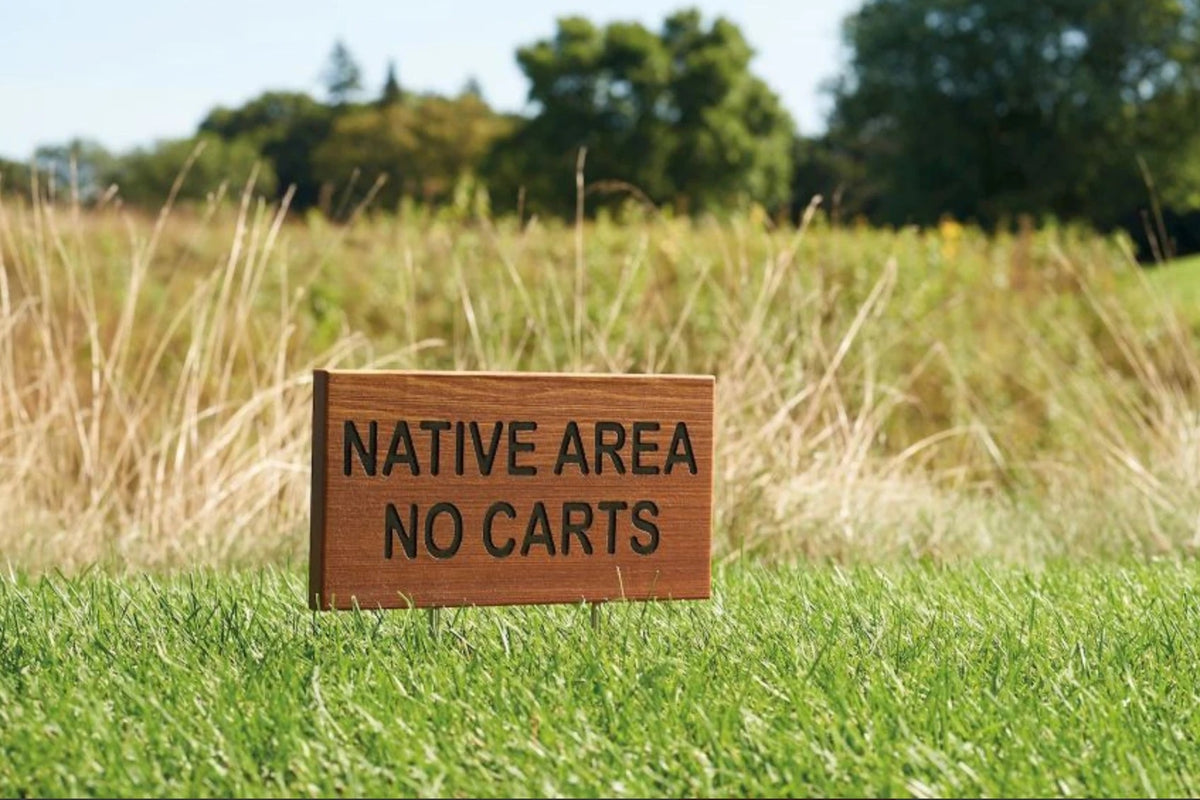 Wooden golf course sign reading Native Area No Carts, with routed painted letters on oiled hardwood, standing in the rough