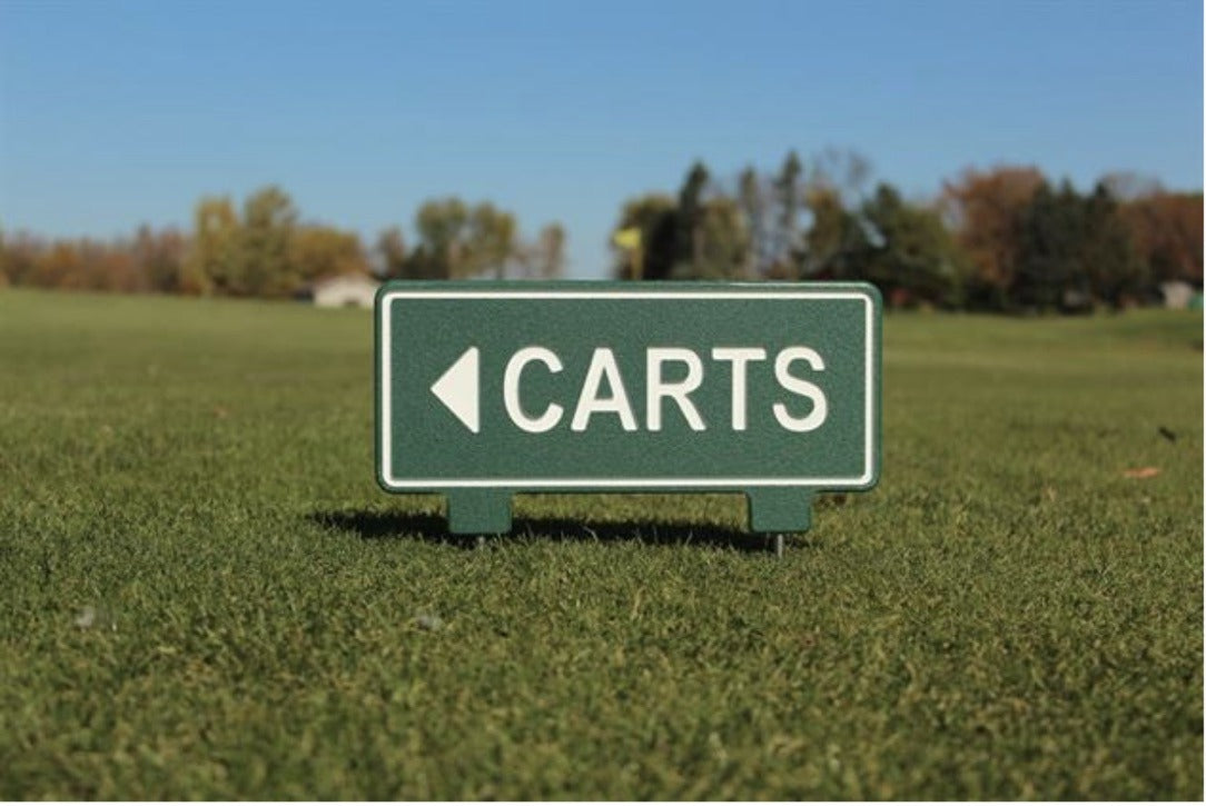 Green golf course directional sign with a white left arrow and the word Carts, standing on the fairway with stainless steel spikes