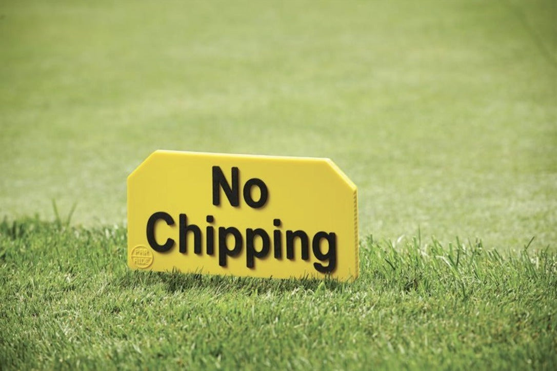 Yellow flexible resin golf course sign with black letters reading No Chipping, standing in the grass with stainless steel spikes