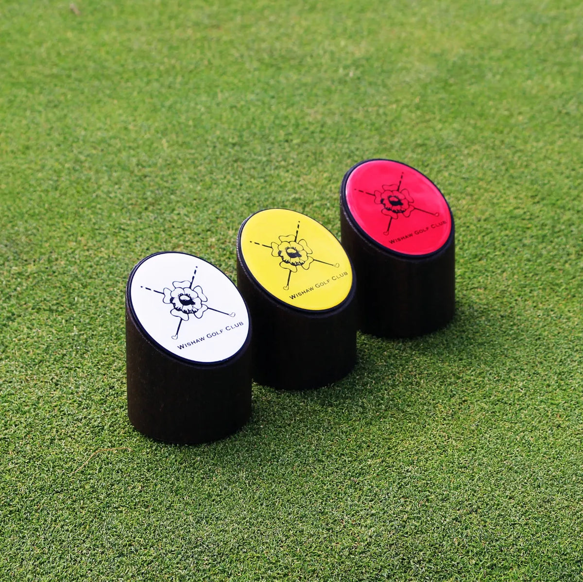 Three short upright golf tee markers with custom resin-domed club logo plates in white, yellow and red